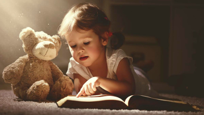 child little girl reading a magic book in the dark home with a toy teddy bear